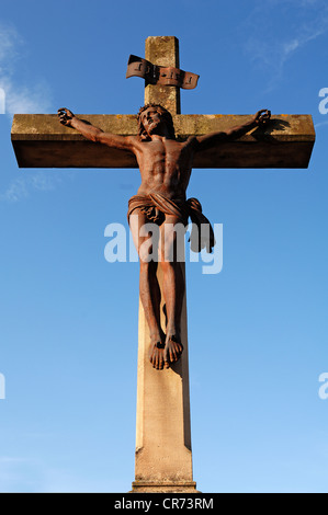 En fonte rouillé statue du Christ sur une croix de pierre, 19e siècle, contre un ciel bleu dans le cimetière de Guebwiller Banque D'Images
