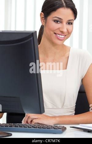 Belle jeune femme latina Hispanic businesswoman ou en costume d'affaires intelligents assis à un bureau dans un bureau à l'aide d'un ordinateur Banque D'Images