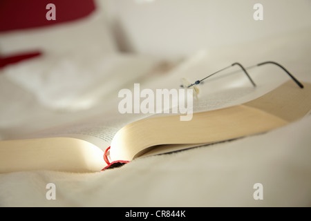 Un livre ouvert avec des lunettes située au-dessus Banque D'Images