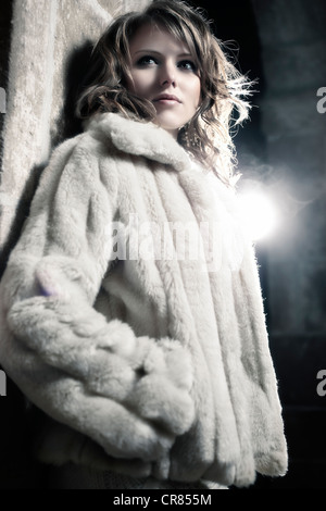 Jeune femme portant un chandail blanc et une veste de fourrure blanche, appuyé sur un mur Banque D'Images