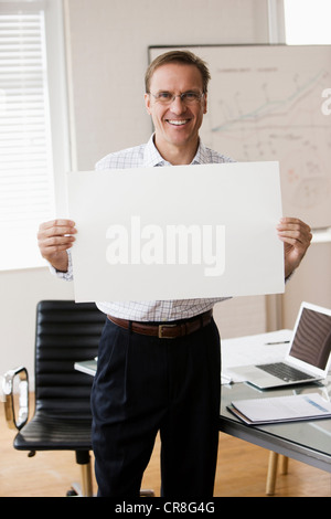 Mature businessman holding blank page in office Banque D'Images