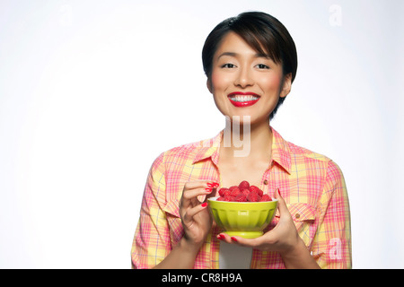 Young woman holding bowl de framboises against white background Banque D'Images
