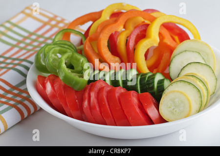 Un bol de tranches de légumes y compris les tomates, salade de poivrons, concombres, courgettes, courge jaune et avec une serviette à rayures Banque D'Images