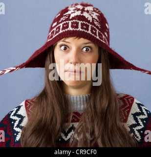 Plaisanterie ludique young woman wearing cap laine pull et posant pour une drôle de studio shot contre un fond bleu clair Banque D'Images