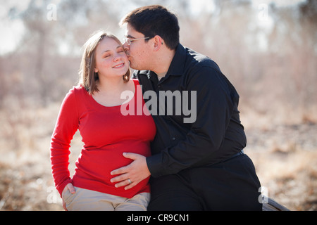 Happy Cute young pregnant couple marié en plein air appuyé contre un journal. Banque D'Images