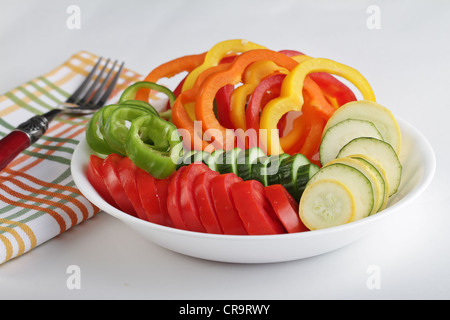 Un bol plein de tranches de légumes y compris les tomates, salade de poivrons, concombres, courges sur un fond blanc avec une serviette à rayures Banque D'Images