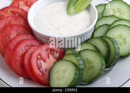 Une vue en gros plan d'une plaque tranches de tomates italiennes et de tranches de concombre sans pépins avec un bol de trempette ranch. Banque D'Images