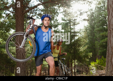 Couple carrying mountain bikes in forest Banque D'Images