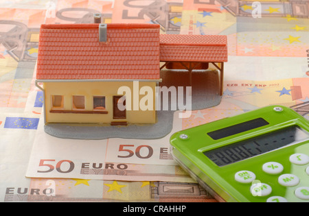 Maison miniature avec un abri sur 50 billets et une calculatrice, image symbolique pour marché de l'immobilier Banque D'Images