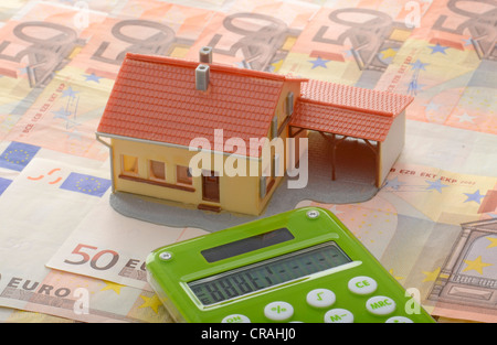 Maison miniature avec un abri sur 50 billets et une calculatrice, image symbolique pour marché de l'immobilier Banque D'Images
