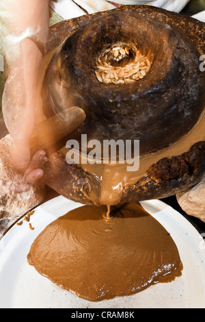 Femme d'Argan torréfié de broyage (Argania spinosa) amandes entre deux meules pour le processus de fabrication traditionnelle Banque D'Images