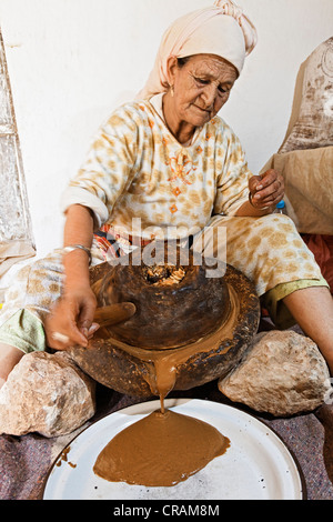 Femme d'Argan torréfié de broyage (Argania spinosa) amandes entre deux meules pour le processus de fabrication traditionnelle Banque D'Images