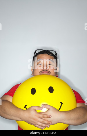 Portrait d'un homme tenant un grand ballon jaune avec symboles smiley Banque D'Images