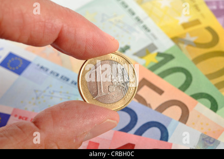 1-pièce en euros tenu entre les doigts devant un ventilateur de divers billets en euros Banque D'Images