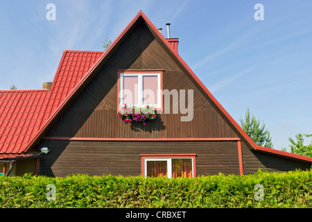 Le toit en plastique rouge privé rural standard petite maison en bois. La production de masse. Clôture couverture conifère Thuja. Sunny fort Banque D'Images