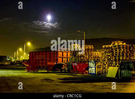 Des poubelles, manqués et des palettes en bois dans une usine de triage à la nuit. Banque D'Images