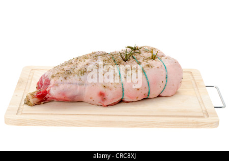 Un gigot d'agneau frais placé sur une planche à découper en bois - studio photo avec un fond blanc Banque D'Images