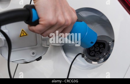 Woman's hand poussant la fiche dans la prise de charge de voiture électrique Suzuki Splash Banque D'Images