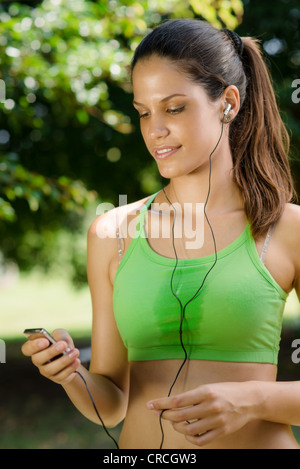 Jeune femme avec un lecteur mp3 faisant la forme physique dans le parc de la ville Banque D'Images