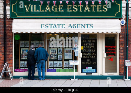 Un couple regarde la fiche dans une fenêtre d'agents immobiliers à Sidcup. Banque D'Images