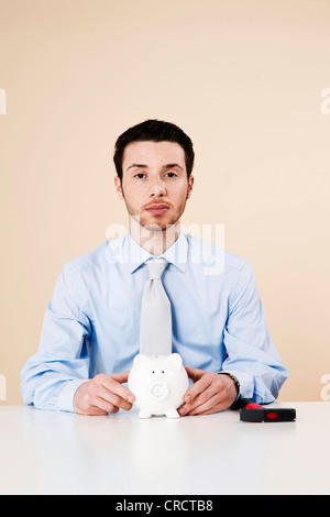 Jeune homme assis en face de Piggy Bank Banque D'Images