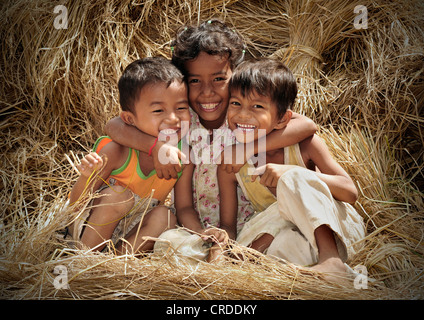 Trois enfants rire assis sur la paille de riz, au Cambodge, en Asie du Sud-Est, l'Asie Banque D'Images
