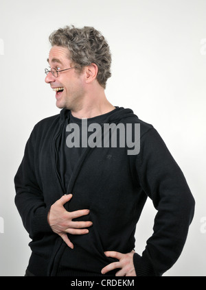 Jeune homme avec des lunettes de rire de bon cœur, une main sur son abdomen Banque D'Images