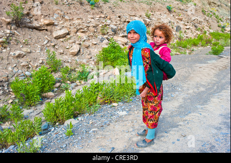 Jeune fille portant un foulard bleu et sa jeune soeur dans un harnais sur son dos, Haut Atlas, Maroc Banque D'Images