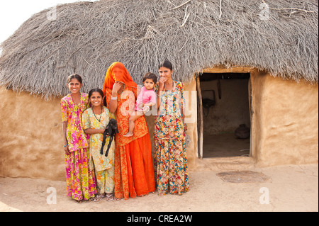 Les filles et les jeunes curieux femme debout devant leur maison, une jeune femme voilée portant un sari est portant son enfant dans Banque D'Images