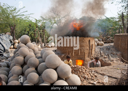 Un four d'argile l'argile pour le tir à l'eau, deux potiers puting plus de bois sur le four, face à l'eau fini empilés Banque D'Images