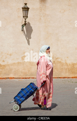 Femme portant une djellaba, une robe traditionnelle, avec un panier, en face de la Medersa Ben Youssef dans la Médina Banque D'Images