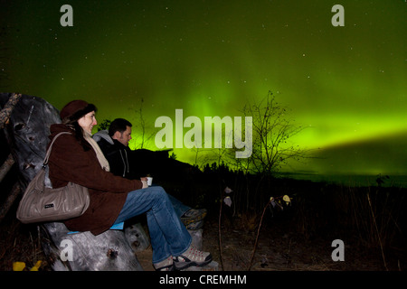 Couple, femme et homme, assis dans une chaise en bois, regardant tourbillonner Northern Lights, aurores polaires, Aurora Borealis, vert Banque D'Images