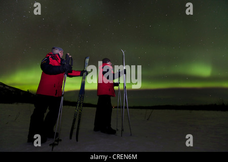 Jeune couple, femme et homme, ski de fond, regardant tourbillonner le nord de lumières polaires, Aurora Borealis, vert Banque D'Images