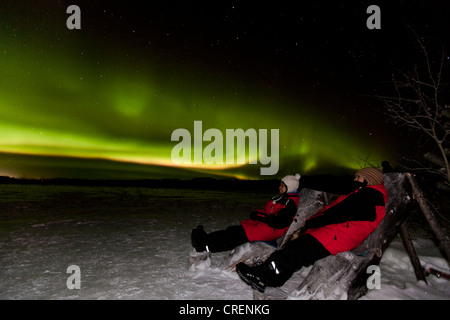 Deux personnes assis dans des chaises en bois, en regardant le pôle nord Green Lights (aurores boréales), près de Whitehorse, Territoire du Yukon Banque D'Images