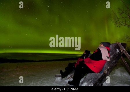 Jeune couple, femme et homme, assis dans une chaise en bois, en regardant le pôle nord Green Lights (aurores boréales), près de Whitehorse Banque D'Images