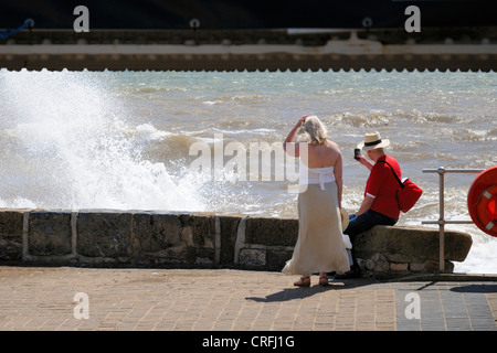 Couple d'âge moyen en regardant les vagues splash contre le mur de la mer à Exmouth Banque D'Images