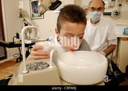 Un garçon se rince à sa bouche avec une solution anti-microbien ayant avant traitement. Banque D'Images