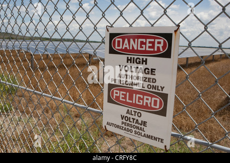 Signe de danger haute tension sur le grillage à la ferme d'énergie solaire au Texas en anglais et espagnol Banque D'Images