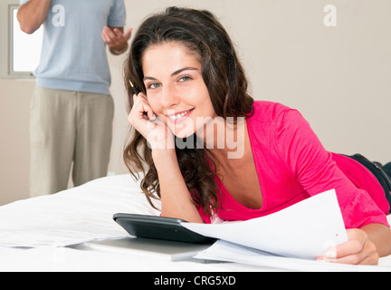 Woman using calculator on bed Banque D'Images