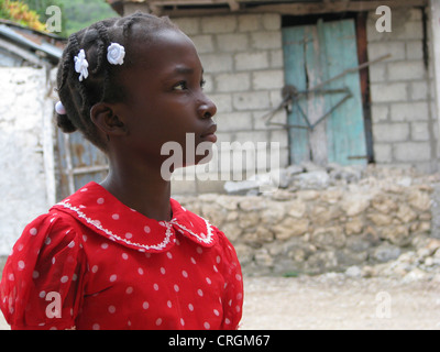 Jeune fille noire à bretelles et robe rouge debout devant de maison simple, Haïti, Grande Anse, Roseau Banque D'Images