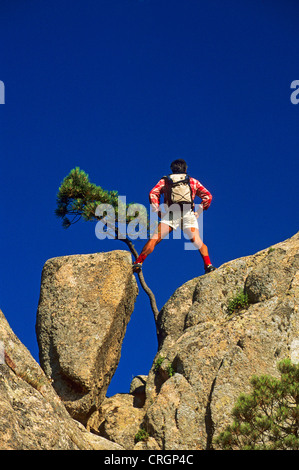 Homme debout les jambes écartées sur rock formation des montagnes de Bavella, France, Corse, aiguilles Banque D'Images