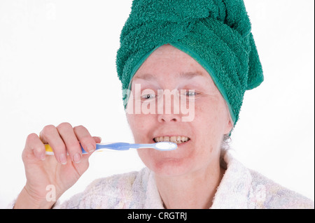 Femme âgée avec une serviette autour de ses cheveux se brosser les dents Banque D'Images