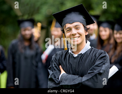 Groupe de diplômés avec un homme debout en souriant au premier plan, tenant son diplôme Banque D'Images