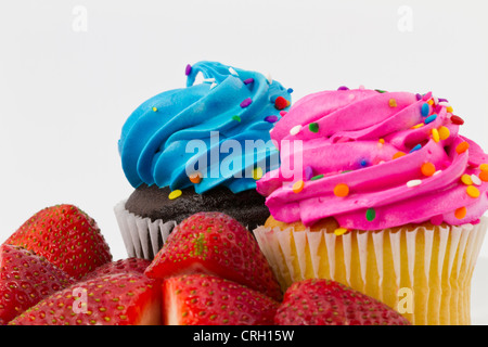 Vanille et chocolat cupcakes avec glaçage rose et bleu et saupoudré, placé derrière les fraises fraîches. Banque D'Images