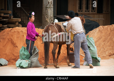 Un homme et une femme le chargement des marchandises sur un cheval, xijiang village miao, Chine Banque D'Images