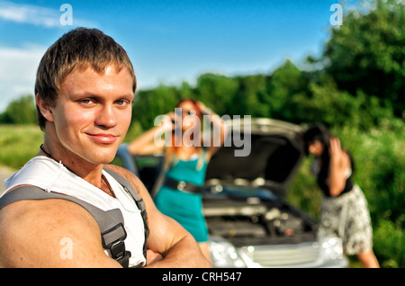 Portrait of handsome mechanic avec deux des femmes sans ressources et casse de voiture sur l'arrière-plan Banque D'Images