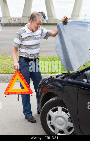 Homme mature avec triangle d'urgence debout devant des véhicules terrestres Banque D'Images