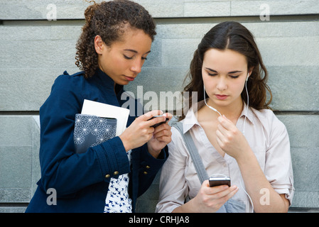 Les jeunes femmes ensemble à l'extérieur, la messagerie texte et listening to MP3 player