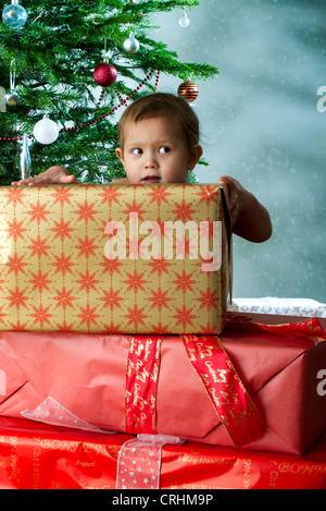 Baby Girl debout derrière la pile de cadeaux de Noël à l'expression espiègle Banque D'Images