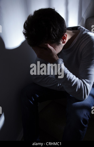Jeune homme assis sur les escaliers, ses mains couvrant son visage. Banque D'Images